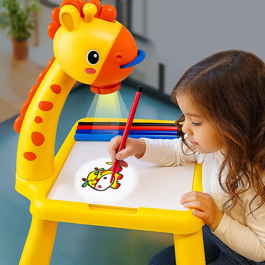 A young child is drawing on a colorful giraffe-shaped children's drawing table. The table has a yellow body, an orange giraffe head, and a white drawing surface, with colored drawing sticks stored on the back.